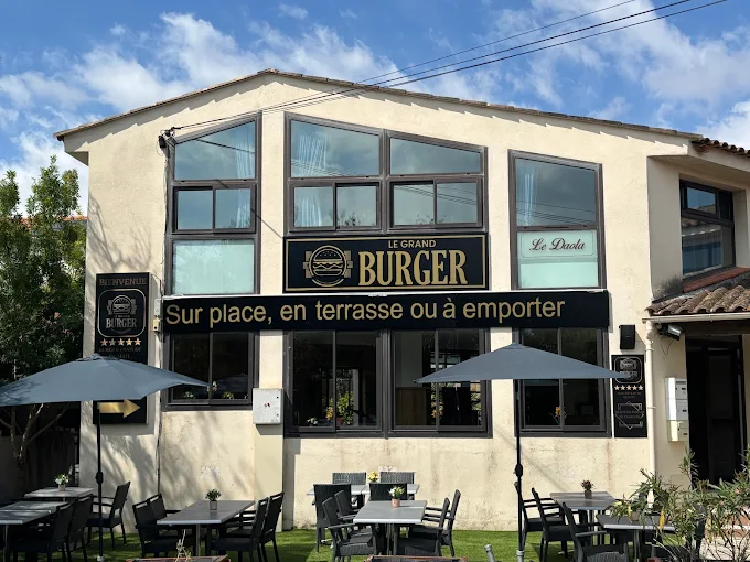 Façade du restaurant Le Grand Burger à Fréjus avec enseigne noir et or, terrasse ombragée et parasols
